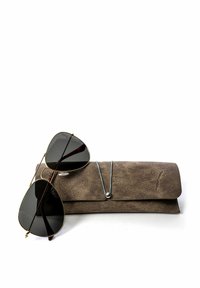 Pilotní sluneční brýle s černými skly položené na hnědém koženém pouzdru. Pouzdro má hladkou texturu a uzávěr na tlačítko s modrým akcentem.