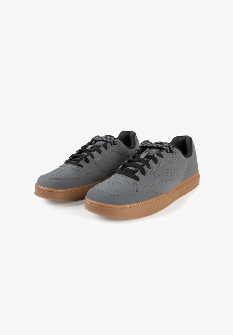 Graue Turnschuhe mit gelochter Oberseite, schwarzen Schnürsenkeln und brauner Gummisohle. Verfügt über dezentes Branding und ein niedriges Design.