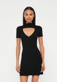 Rochie neagră, tricotată cu dungi, mâneci scurte, decolteu decupat cu un accent argintiu. Croială mulată și lungime deasupra genunchiului.