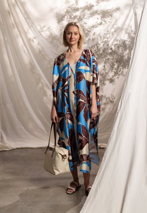Kaftán fluido en azul, marrón y crema con patrones de hojas, con escote en v y mangas sueltas. Bolsa beige con asas marrones.