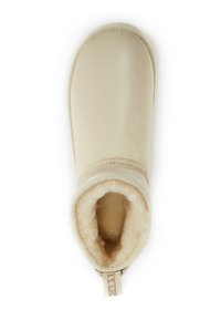 Bota de cuero beige con un suave forro de piel de oveja, punta redonda y un lazo de tela en la parte trasera para facilitar el calzado. Textura suave.