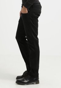 Svarta slim-fit byxor i denim med medelhög midja, sidofickor och bakfickor samt en slät yta. Bärs med svarta skor.