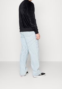 Černá sametová mikina s dlouhým rukávem, volný střih, v kombinaci se světle modrými širokými džíny s prohnutými švy a černými teniskami.