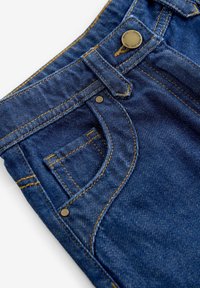 Gros plan sur la poche avant d’un jean en denim bleu avec des rivets en laiton, une couture orange et un bouton métallique à la ceinture.