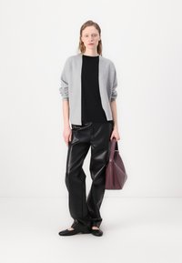 Šedý pletený cardigan přes černý top, spárovaný s černými koženými kalhotami a černými plochými botami, držící burgundskou kabelku. Hladké textury, moderní design.