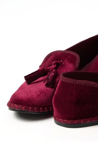 Pantofole in velluto bordeaux con una consistenza morbida, caratterizzate da un dettaglio con nappina e un bordo cucito a contrasto. Design con chiusura sul retro e interno liscio.