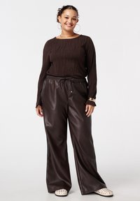 Haut à manches longues côtelé marron avec un col rond, associé à un pantalon large en simili cuir marron et des mocassins crèmes à clous.