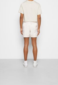 Lyhythihainen beige paita, satiiniset kermanväriset shortsit, joissa on kiristettävä vyötärö, yhdistettynä valkoisiin korkeisiin tennareihin. Sileä pinta ja yksinkertainen muotoilu.