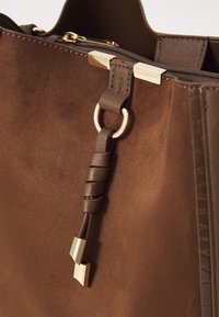 Borsa a tote in suede marrone con una finitura texture, caratterizzata da un accento in metallo dorato e un manico in pelle con dettaglio a nodo.