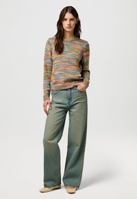 Multicolored knit sweater with textured stripes, paired with light-wash wide-leg jeans and beige flats. Relaxed fit and ribbed cuffs.