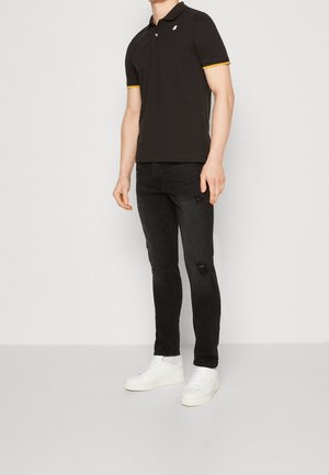 Black polo shirt with yellow accents, short sleeves, and a collar, paired with black distressed jeans and white sneakers.