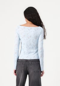 Light blue lace top with long sleeves, featuring a floral pattern and a wide neckline. Paired with gray, high-waisted jeans.