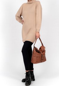Robe-pull beige tricotée avec col montant et manches longues, associée à des leggings noirs et des bottes noires à lacets ; tenant un sac en cuir marron.