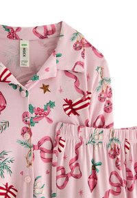 Pink cotton pajama set featuring a collared shirt and elastic-waist pants. Pattern includes festive elements like bells, bows, and holly.