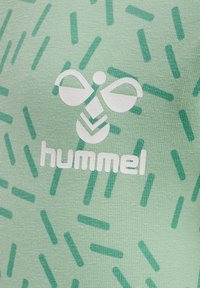 Tissu en coton vert avec un motif texturé de rayures diagonales vertes plus foncées et un logo blanc représentant une abeille stylisée et le mot "hummel."