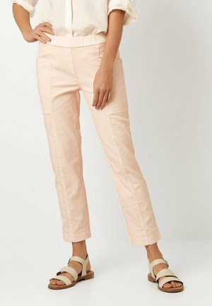 Hellrosa, taillierte Hose mit elastischem Bund und aufgesetzten Taschen vorne. Getragen mit beigen Sandalen, die mehrere Riemen und eine flache Sohle haben.