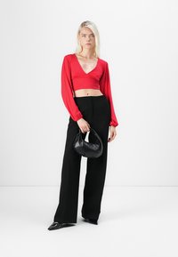 Rode langemouwen cropped top met een diepe V-hals, gecombineerd met hoge zwarte wijde broekspijpen en een kleine zwarte handtas.