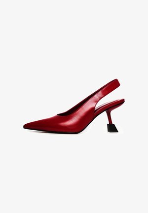 Női lábak fényes piros slingback hegyes orrú magas sarkú cipőben, egyedi négyzet alakú tűsarkakkal, fehér háttéren.