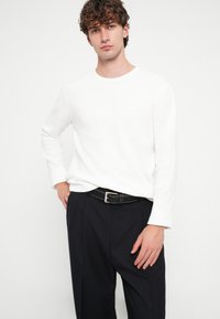 Fehér hosszú ujjú ing kerek nyakkivágással, sötét, szabott nadrággal és fekete övvel, ezüst fém díszítéssel párosítva.