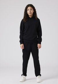 Zwarte hoodie met een relaxte pasvorm en ribgebreide manchetten, gedragen met zwarte joggingsbroek. Gemaakt met witte sneakers.