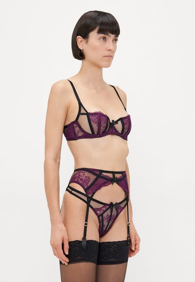 Paarse en zwarte kanten lingerieset met een bralette met doorzichtige cups, decoratieve strikjes en hooggesneden jarretelbriefjes met banddetails.