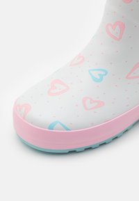 White rubber boot with pink and blue heart patterns, pink sole, and light blue accents. Smooth texture with a rounded toe design.