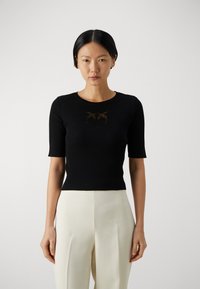 Top negro de manga corta con cuello redondo, que presenta un sutil diseño gráfico en marrón. Combinado con pantalones de pierna ancha de color claro.