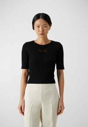 Top corto a maniche corte nero a coste con scollo rotondo, caratterizzato da un sottile design grafico marrone. Abbinato a pantaloni palazzo chiari.