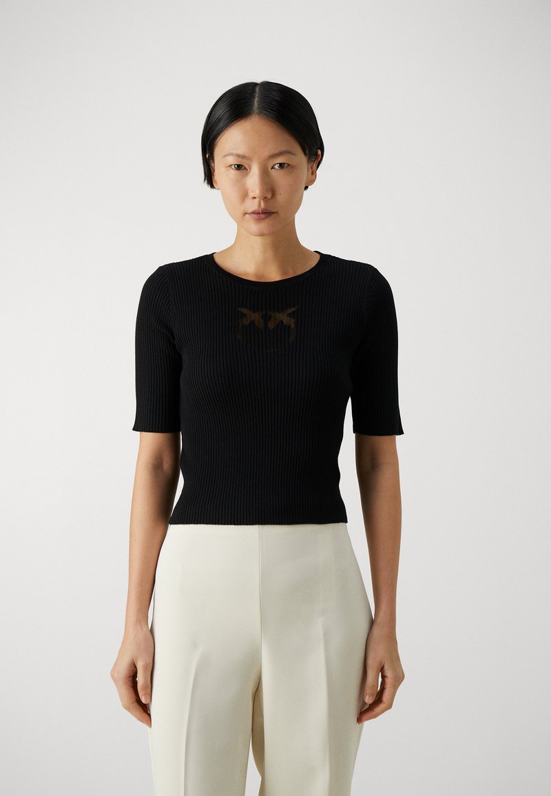 Top negro de manga corta con cuello redondo, que presenta un sutil diseño gráfico en marrón. Combinado con pantalones de pierna ancha de color claro.
