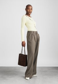 Top de punto amarillo claro con botones, combinado con pantalones grises plisados. Los accesorios incluyen un bolso tote marrón y zapatos blancos de punta afilada.