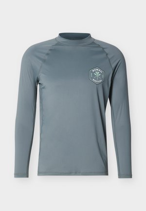 Gaiši zilganpelēka garroku aizsargkrekls ar apaļu izgriezumu un sešstūra formālu "Hawaii Rip Curl" logotipu kreisajā krūtīs.