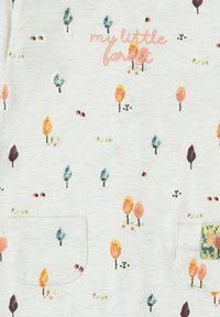 Tela blanca con un tema de bosque que presenta árboles coloridos y pequeños patrones. Texto rosa que dice "mi pequeño bosque." Dos bolsillos delanteros.