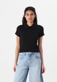 Svart pikétröja med korta ärmar, utrustad med en knappslå och en strukturerad krage. Bärs tillsammans med ljusblå högmidjade jeans.