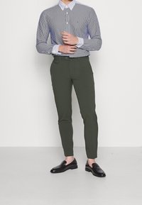 Modrá a bílá pruhovaná košile s knoflíky spárovaná s olivově zelenými slim-fit kalhotami a černými mokasíny, s neformálním a přiléhavým designem.