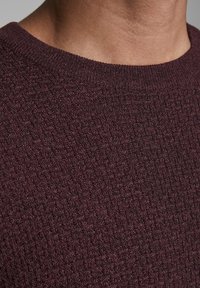 Bordowy materiał o fakturze z dzianym wzorem, z okrągłym dekoltem i gładkimi krawędziami. Zbliżenie na szczegóły materiału.