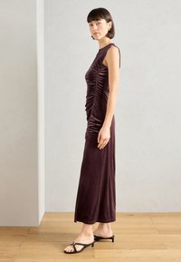 Μωβ αμάνικο φόρεμα με ρυτίδες στο πλάι, εφαρμοστή σιλουέτα και μήκος μέχρι το πάτωμα. Συνδυασμένο με μαύρες σανδάλια με λουριά και τακούνια.