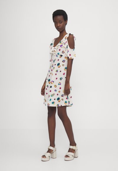 Rochie albă cu un model colorat și stropit, cu mâneci volanate off-shoulder, tiv până la genunchi, asortată cu sandale albe cu toc gros.
