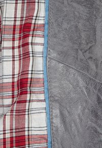 Un tessuto grigio testurizzato è su un lato, in contrasto con un motivo a quadri rosso e bianco dall'altro, bordato da un rifinitura azzurro chiaro.