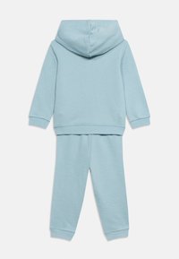Σετ με ανοιχτό μπλε φούτερ με κουκούλα και παντελόνι φόρμας για μικρό παιδί, εμφανίζεται από πίσω σε λευκό φόντο.