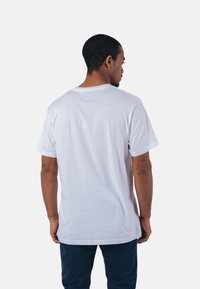 T-shirt en coton blanc avec des manches courtes, col rond et une petite étiquette en haut du dos. Texture lisse avec une coupe décontractée.