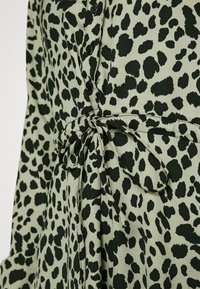 Blouse verte à imprimé léopard noir, avec fermeture boutonnée et taille nouée. Tissu léger avec une texture lisse.