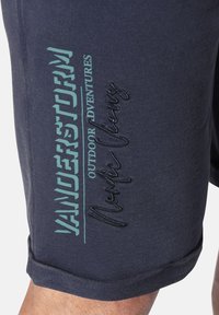 Navy blue shorts featuring contrasting turquoise and black text, with a rolled hem and a soft fabric texture, ideal for outdoor activities.