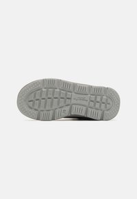 Sneakerzool in grijs rubber, met een gestructureerd patroon van groeven en richels voor grip. Gestempeld logo en maatdetails zichtbaar.