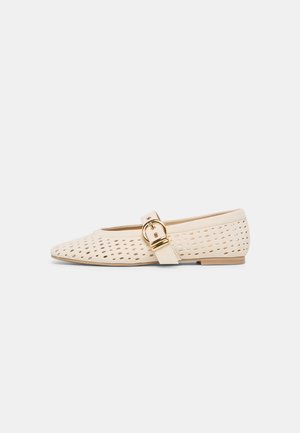 Beige flat shoe with pointed toe, perforated upper, and decorative gold buckle strap on side.