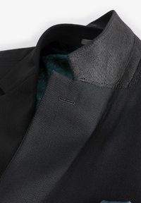 Colletto di giacca elegante nero con tessuto grigio testurizzato. Interno con fodera verde acqua e motivo geometrico. Include dettagli cuciti.