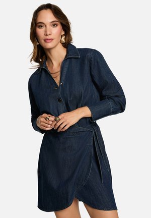 Robe en denim à manches longues, col et fermeture à boutons. Présente une ceinture à la taille et un ourlet légèrement incliné, de couleur bleu indigo foncé.