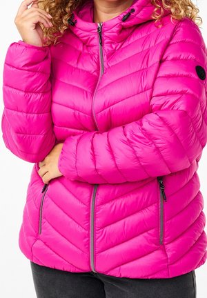 Femme portant une veste matelassée rose vif avec fermeture éclair devant et poches, tenant le col d'une main.
