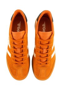 Baskets en daim orange avec des rayures et lacets blancs, affichant un accent noir au niveau du talon. Semelle en caoutchouc plate et logo sur la languette.