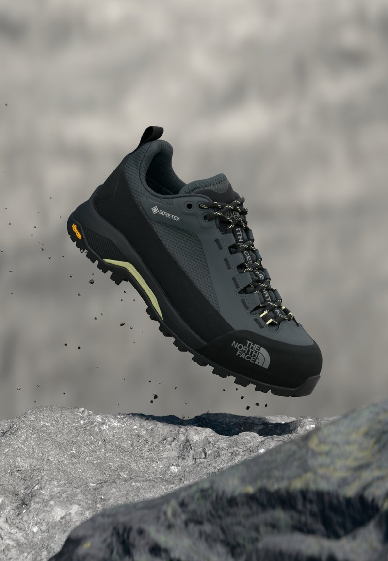 Fekete túracipő GORE-TEX anyagból, szürke texturált részletekkel, gumitalppal és masszív tapadási mintázattal. Fűzővel és logórészlettel ellátva.