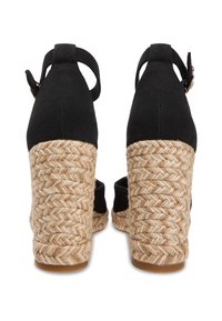 Μαύρα υφασμάτινα τακούνια εσπαντρίγιες με βάση από πλεγμένο τζούτ. Τα παπούτσια έχουν λουράκια στον αστράγαλο και υφή φινιρίσματος, με φυσικού χρώματος σόλα.